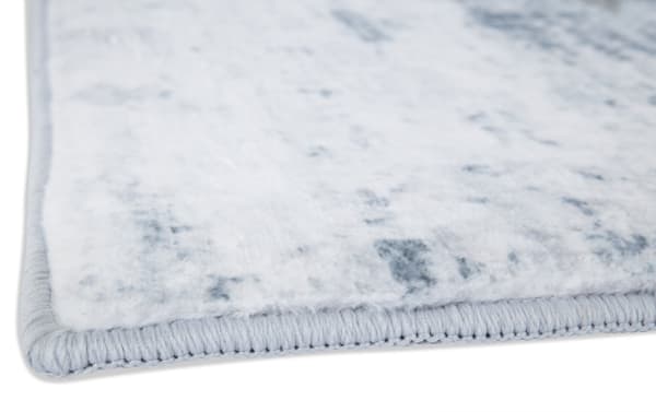 Close-up of a light gray and white textured area rug corner with tightly stitched edges, showcasing soft fabric and durable binding.