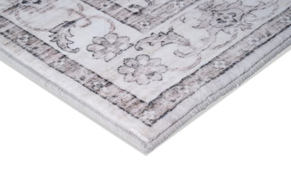 Corner close-up of a beige and gray floral patterned area rug with a soft, plush texture and stitched edges.