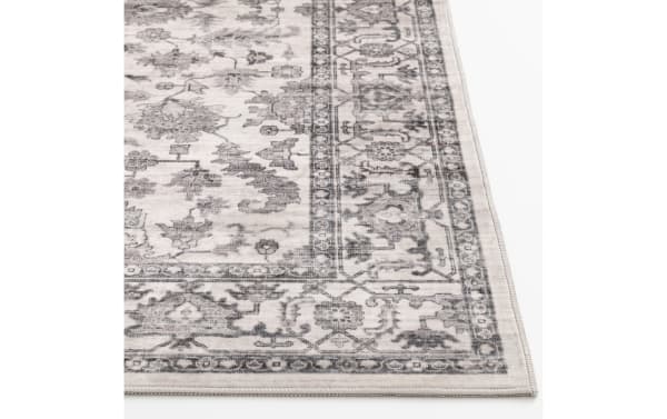 Vintage-style area rug with a distressed gray floral pattern on a cream background, featuring a detailed border and low pile texture.