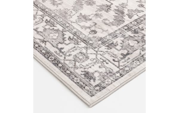 Corner of a beige and gray vintage-style area rug with intricate floral and geometric patterns, featuring a soft, woven texture.