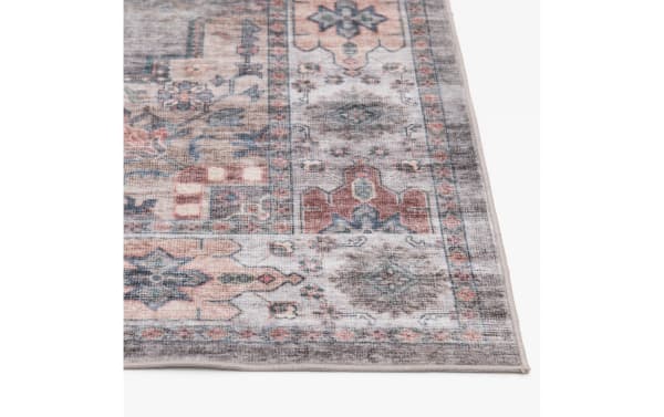 Vintage-style area rug corner with muted pastel colors including dusty pink, blue, and gray, featuring intricate floral and geometric patterns on a soft woven fabric.