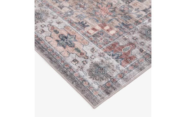 Corner view of a vintage-style area rug with muted earth tones, featuring geometric and floral patterns in beige, rust, blue, and gray colors.