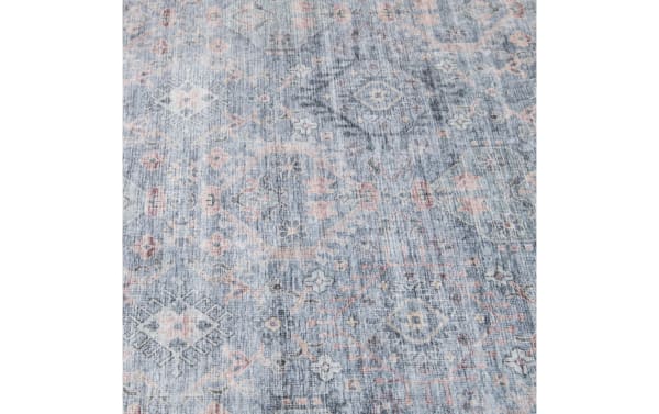 Vintage-style area rug with faded blue background, intricate geometric and floral patterns in soft pink, beige, and gray tones, textured fabric.