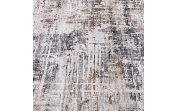 Abstract patterned area rug with a distressed, weathered look in muted tones of gray, beige, and brown, featuring a textured, vintage style design.