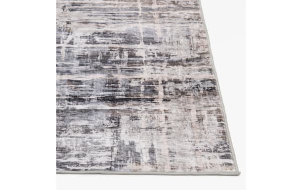Area rug with a distressed abstract pattern in shades of gray, beige, and black, featuring a low-pile texture and stitched edges.