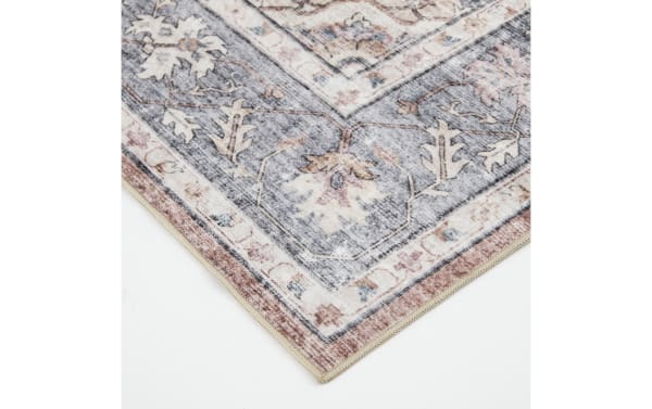 Corner of a vintage-style area rug with floral patterns in muted gray, beige, and dusty rose tones, featuring a soft woven texture and decorative border.