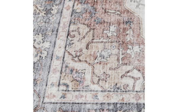 Vintage-style area rug corner with muted floral and vine patterns in beige, dusty rose, and gray tones, showcasing a distressed texture.