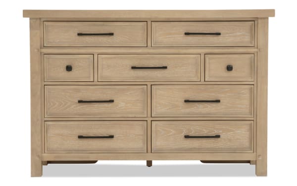 Light wood dresser with nine drawers featuring black metal handles and knobs, showcasing a rustic, farmhouse style storage solution.