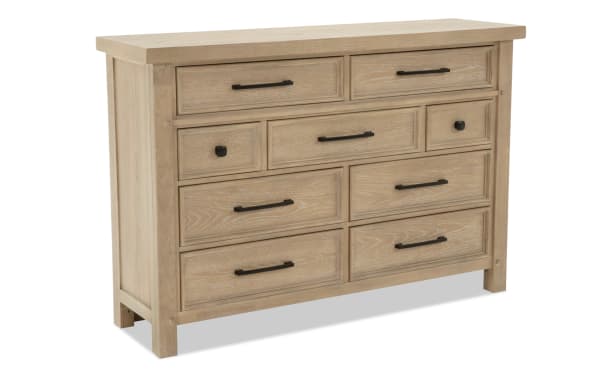 Light wood dresser with nine drawers featuring black metal handles and knobs, showcasing a rustic, farmhouse style storage solution.