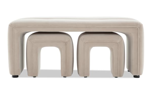 Beige upholstered nesting stools set featuring a large rectangular bench with two smaller arched stools underneath, designed for modern living spaces.