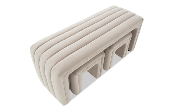 Beige velvet nesting stools with a modern, ribbed design, featuring three sizes that fit neatly under each other for space-saving seating.
