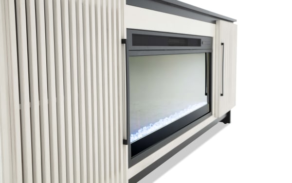 Modern electric fireplace with a black frame, clear glass front, and white decorative stones, set in a light wood cabinet with vertical grooves and black handles.