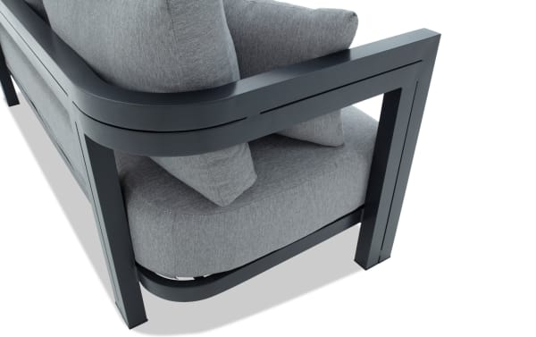 Modern outdoor sofa corner with dark gray powder-coated metal frame and thick light gray fabric cushions, emphasizing durability and contemporary design.