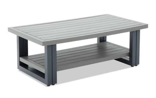 Modern rectangular outdoor coffee table with gray slatted wood top and lower shelf, supported by dark gray metal frame legs.