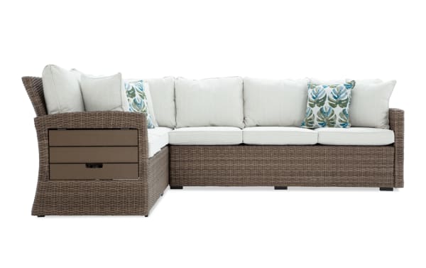 Outdoor sectional sofa with brown wicker frame, beige cushions, and two decorative leaf-patterned throw pillows, designed for patio seating.
