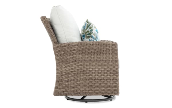 Outdoor swivel chair with taupe woven rattan frame, beige cushions, and a decorative blue and green leaf-patterned pillow.
