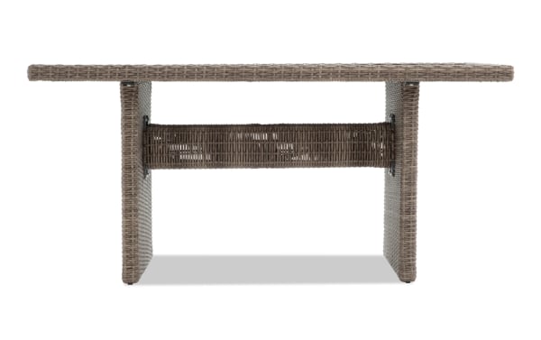 Rectangular outdoor dining table with woven rattan texture in taupe color, featuring sturdy side panels and a horizontal support beam.