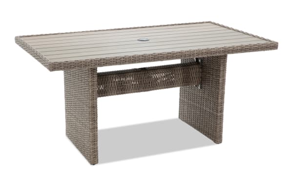 Rectangular outdoor wicker patio dining table with beige slatted top, woven rattan base, and central umbrella hole, suitable for garden seating.