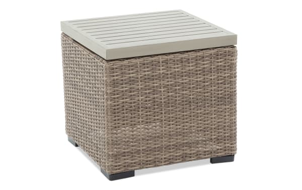 Square outdoor side table with beige synthetic wicker base and light gray slatted wood top, featuring black feet for stability.