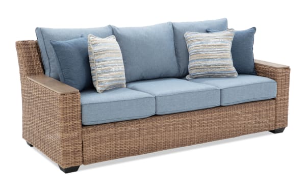 Outdoor wicker sofa with light blue cushions and striped throw pillows, featuring a sturdy woven rattan frame and wooden armrests.