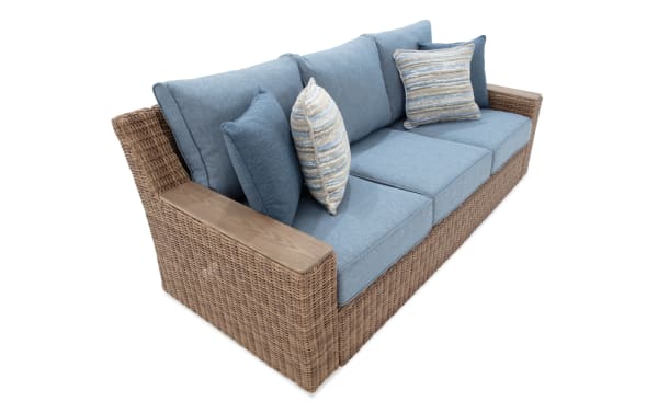 Outdoor wicker sofa with blue fabric cushions and striped throw pillows, featuring wooden armrests and a modern, comfortable design.