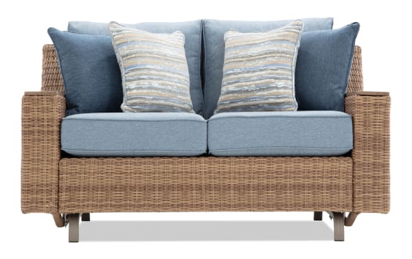 Outdoor loveseat with woven rattan frame, light blue cushions, and decorative striped and solid blue throw pillows, suitable for patio seating.