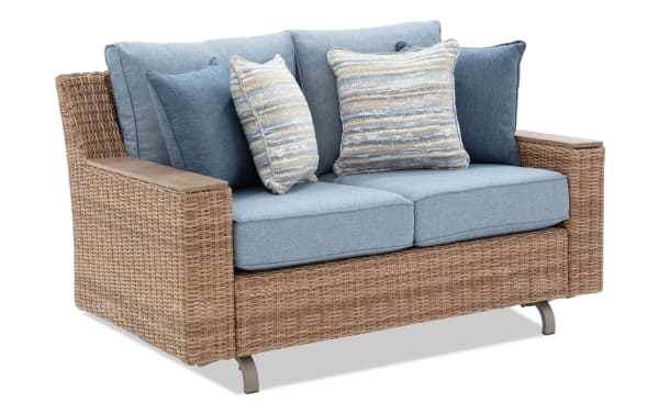 Outdoor loveseat sofa with woven rattan frame, light blue cushions, and striped blue and beige throw pillows, modern patio furniture.