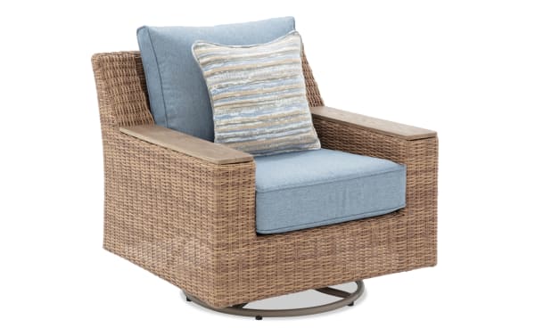 Outdoor swivel armchair with light blue cushions, woven rattan frame, wooden armrests, and striped decorative pillow.