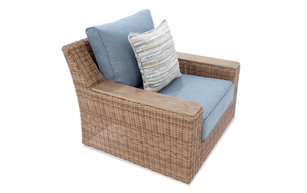 Wicker armchair with light blue fabric cushions and a striped lumbar pillow, featuring wooden armrests and a modern woven design.