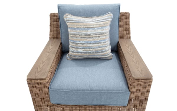 Wicker armchair with light blue fabric cushions and a square decorative pillow featuring horizontal stripes in blue, beige, and gray tones.