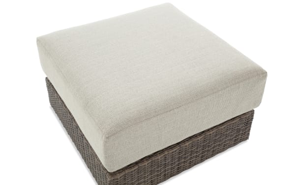 Transitional Modular Bob® Beige & Brown Wicker Outdoor Ottoman with rust-proof aluminum frame, all-weather wicker base, and plush beige polyester cushion.
