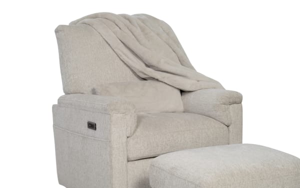 Light gray upholstered recliner chair with matching ottoman, featuring a soft plush throw blanket and lumbar pillow for added comfort.