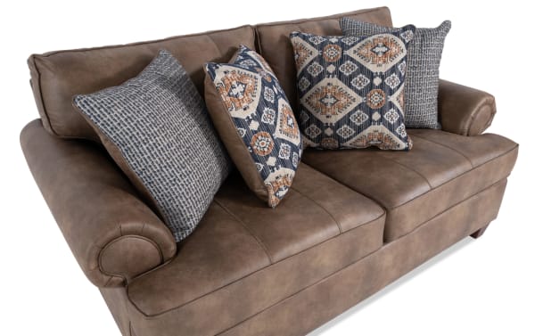 Raleigh Cognac 76'' loveseat in traditional style with brown faux leather polyester upholstery, rolled arms, and patterned accent pillows.