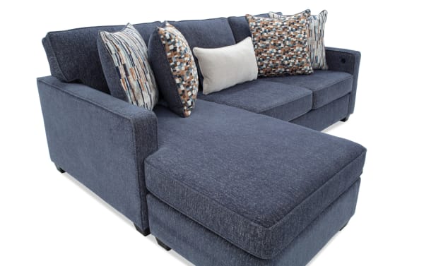 Modern sectional sofa with dark blue fabric upholstery, featuring a chaise lounge on the left side and multiple patterned and solid throw pillows for added comfort and style.
