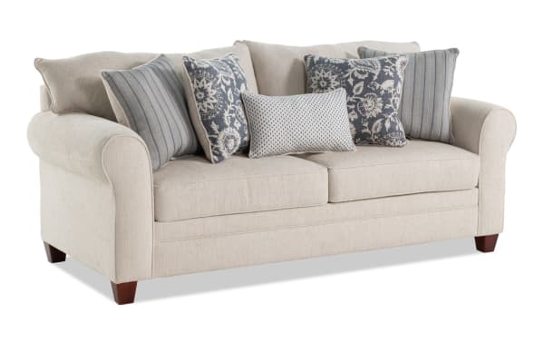 Portland Beige 85'' transitional sofa with soft polyester fabric upholstery, rolled arms, wooden legs, and five blue-patterned accent pillows.
