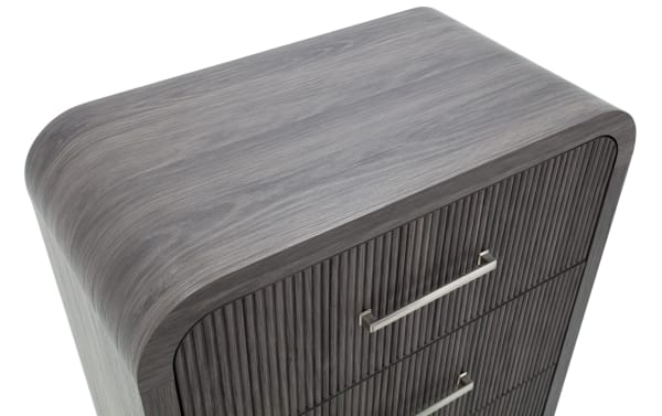 Modern gray wooden dresser with rounded edges and vertical slat drawer fronts, featuring sleek metal handles for a contemporary bedroom.
