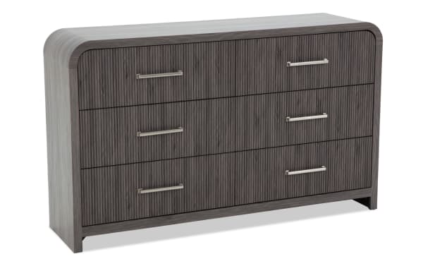 Modern dark gray wood dresser with six drawers featuring vertical grooves and sleek silver metal handles, rounded edges, and a light gray top surface.