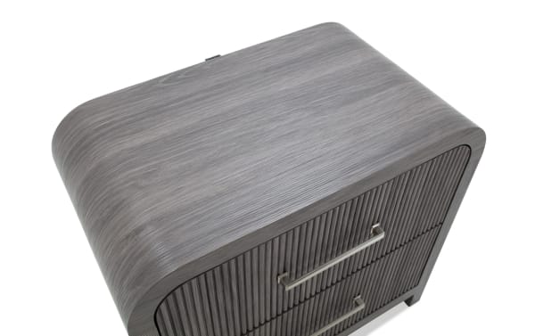 Modern gray wooden nightstand with rounded edges, two ribbed front drawers, and sleek metal handles, ideal for bedroom storage.