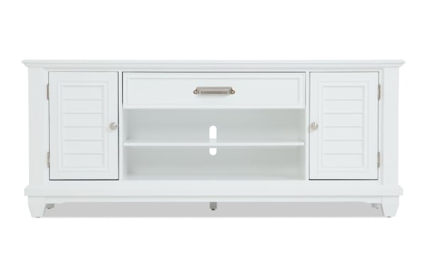 White wooden TV stand with two shutter-style cabinets, a central drawer with metal handle, and open shelving for media devices.
