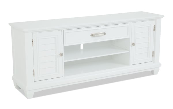 White wooden TV stand with two shutter-style cabinet doors, one central drawer with metal handle, and two open shelves for media devices.