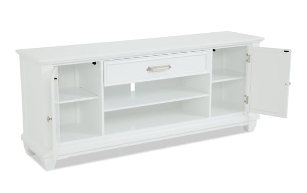 White wooden sideboard with two open doors, one drawer with metal handle, and multiple shelves for storage, featuring a classic design.