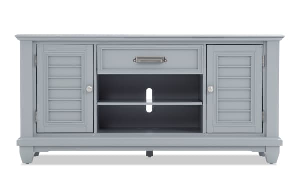Gray wooden TV stand with two shutter-style cabinet doors, one center drawer, and open shelving with cable management hole.