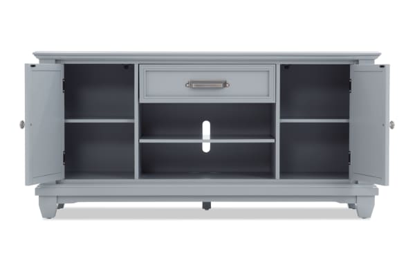 Gray wooden TV console cabinet with two open side doors, central drawer, multiple shelves, and cable management hole in back panel.