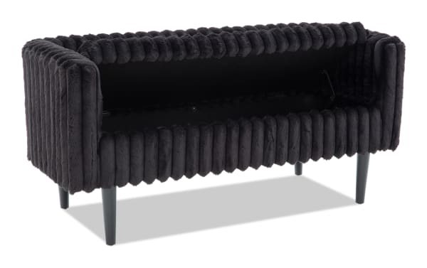 Black plush velvet storage bench with vertical ribbed upholstery, rectangular shape, open top lid, and slim black legs, ideal for living room seating and storage.