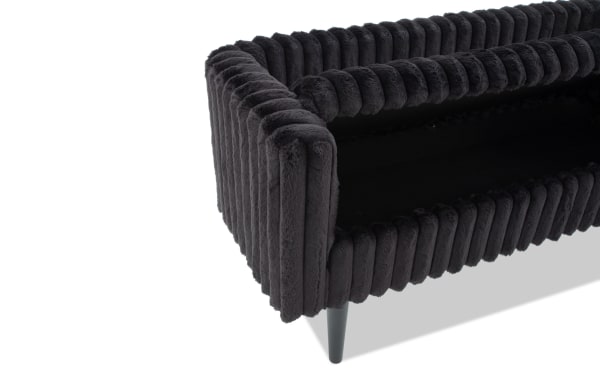 Close-up of a modern black velvet sofa armrest with ribbed texture and tapered black legs, showcasing plush upholstery and contemporary design.