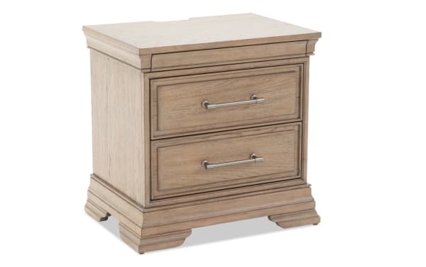 Wooden two-drawer nightstand with a light oak finish, brushed metal handles, and decorative molding, suitable for bedroom storage.