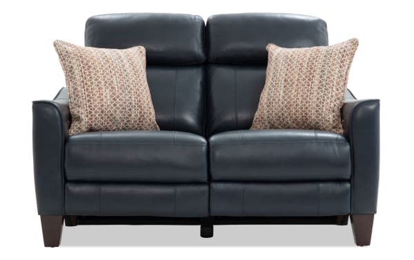 Dark blue leather loveseat with two patterned beige throw pillows, featuring padded armrests and wooden legs, ideal for modern living rooms.