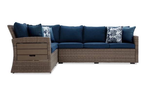 Outdoor sectional sofa with brown wicker frame and navy blue cushions, featuring floral and solid throw pillows, designed for patio seating.