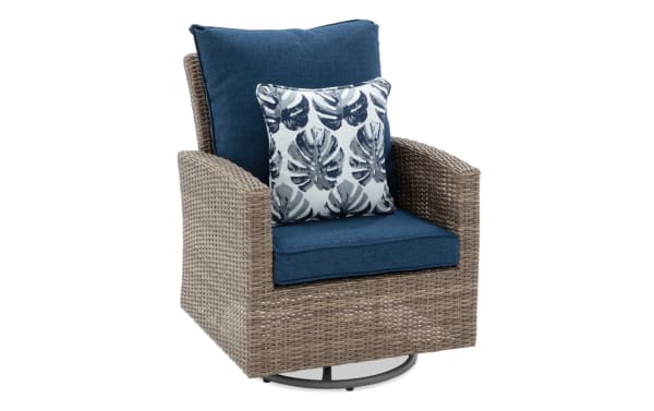 Outdoor swivel armchair with woven rattan frame, blue cushions, and a decorative leaf-patterned throw pillow, ideal for patio seating.