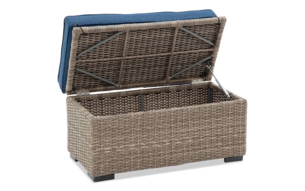 Wicker outdoor storage bench with a blue cushioned lid, featuring a hydraulic lift mechanism and a spacious interior for garden or patio use.